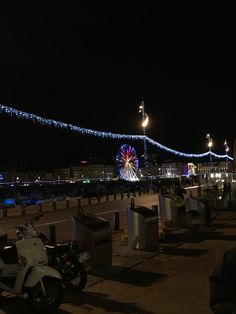 a ferris wheel is lit up in the night sky near some parked scooters