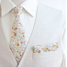 a man wearing a white suit with a floral tie and pocket square on his lapel