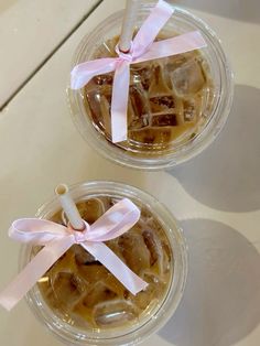 two cups filled with ice cream and topped with pink ribbon on white table top next to each other