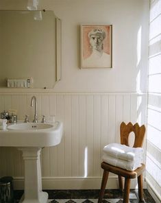 a white sink sitting next to a wooden stool in a bathroom under a painting on the wall