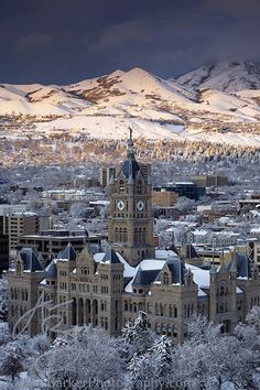 a large building with a clock on the top and snowy mountains in the back ground