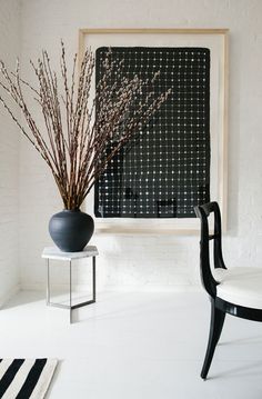 a black vase sitting on top of a white table next to a chair and wall