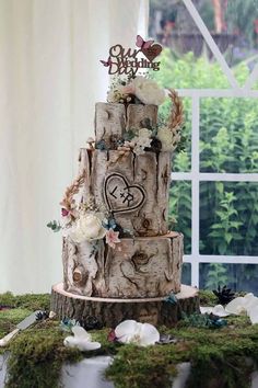 a three tiered wedding cake with flowers and hearts on it is surrounded by moss