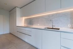 an empty kitchen with white cabinets and marble counter tops, along with a sink in the middle