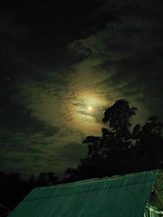 the full moon shines brightly in the night sky over a green roofed building and trees