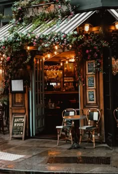 the outside of a restaurant with tables, chairs and plants growing on the building's windows