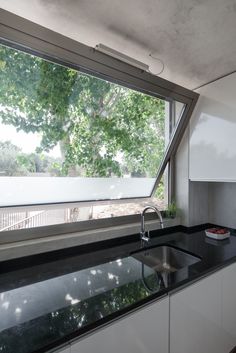 a modern kitchen with black counter tops and white cupboards under a large open window