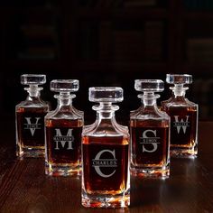 four decante bottles are lined up on a table with the labels for three different types of whiskeys