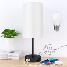 a white lamp sitting on top of a wooden table next to a phone and a plant