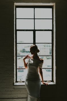 a woman standing in front of a window wearing a white dress and looking out the window