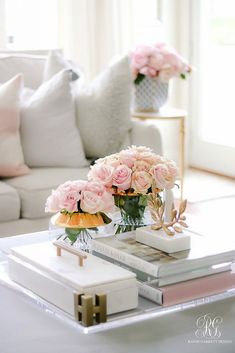 pink roses are in vases on a coffee table with books and magazines next to it