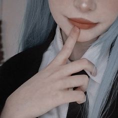 a woman with blue hair is wearing a black jacket and holding her finger to her chin