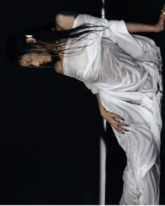 a woman with long hair standing in front of a black background wearing a white dress