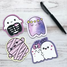 four stickers with different designs on them and a pen next to it, sitting on a wooden surface