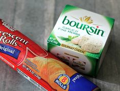 an assortment of cheeses and rolls on a wooden table next to a carton of crescent rolls