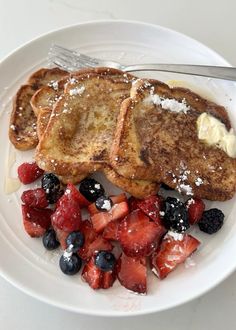 french toast with berries, blueberries and powdered sugar on a white plate next to a fork