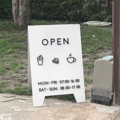 an open sign sitting on the side of a road next to a trash can and garbage can