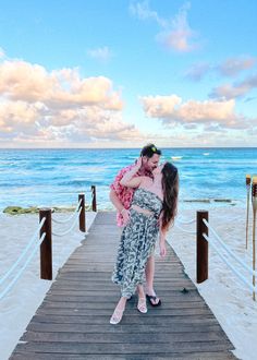 a man and woman kissing on a pier near the ocean with clouds in the sky