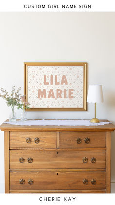 Custom girl name sign with a floral background in a gold frame, personalized with the name "Lila Marie," displayed on a vintage wooden dresser with decorative vases and a lamp, perfect for timeless and elegant nursery decor or children's room wall art. Hobby Lobby Baby Girl Nursery, Name Above Crib, Floral Name Sign, Carousel Theme, Gender Neutral Nursery Design, Nursery Color Scheme, Feminine Colors, Newborn Room, Whimsical Nursery