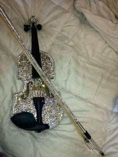 a violin laying on top of a bed covered in white sheets and silver sequins