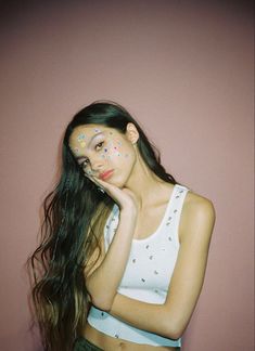 a woman with long hair and face paint posing for a photo in front of a pink wall