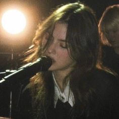 a woman singing into a microphone while standing next to a man on a stage with lights behind her