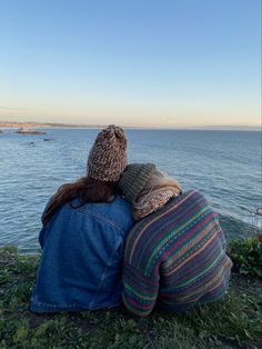 two people sitting next to each other looking out over the water at the shore line