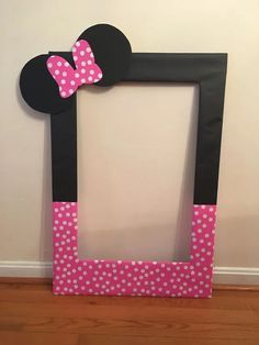 a minnie mouse frame with pink polka dots and a bow on the top, sitting in front of a white wall