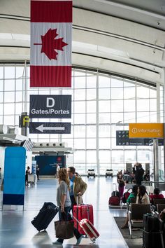 people are walking through an airport with their suitcases in hand and canadian flag hanging from the ceiling