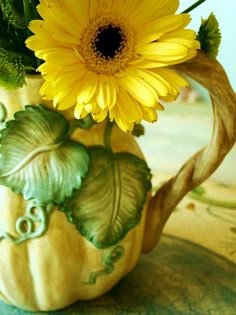 a yellow flower in a green vase on a table with other flowers and leaves around it