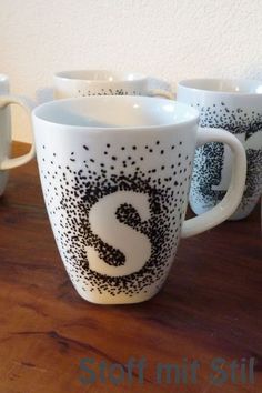 four coffee mugs with black and white designs on them sitting on a wooden table