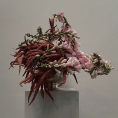 a white vase filled with lots of flowers on top of a table next to a wall