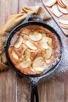 an apple pie in a cast iron skillet with powdered sugar on the side