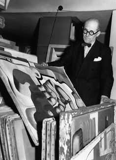 a man in a suit and glasses is looking at an art work on the easel