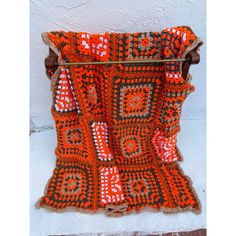 an orange and black crocheted blanket sitting on top of a wooden stand next to a white wall