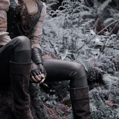 a woman sitting on top of a tree stump in the middle of a forest wearing boots