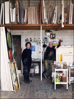 two people standing next to each other in front of bookshelves and shelves with paintings on them