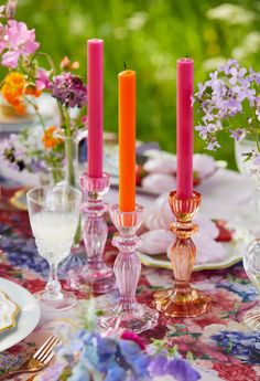 a table topped with pink candles and plates filled with flowers on top of a floral covered table cloth