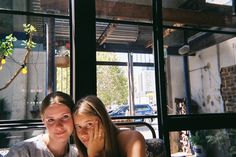 two young women sitting next to each other in front of a glass window with cars outside