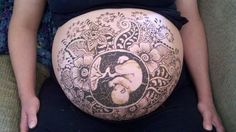 a pregnant woman sitting on a couch with her belly covered in an intricately designed tattoo