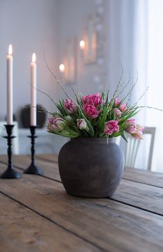 a vase with pink flowers on a wooden table next to two black candles and one white candle