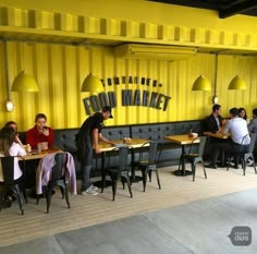 people sitting at tables in front of a yellow wall with the words food market on it