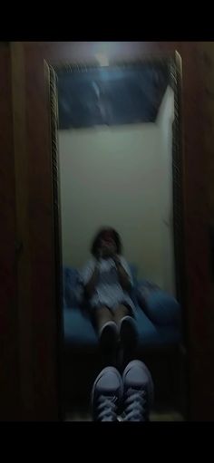 a person sitting in front of a mirror with their feet up on the floor and one leg hanging down