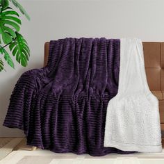 a purple and white blanket sitting on top of a couch next to a potted plant