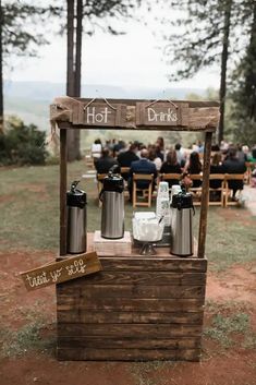 an outdoor bar set up for a wedding with drinks on the table and people sitting in chairs behind it