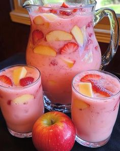 three glasses filled with fruit sitting next to an apple and strawberry milkshake in front of a pitcher