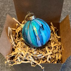 a blue ornament in a box with shredded paper