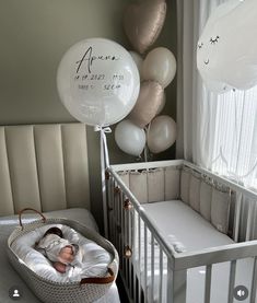 a baby in a crib next to balloons and a bed with a white blanket