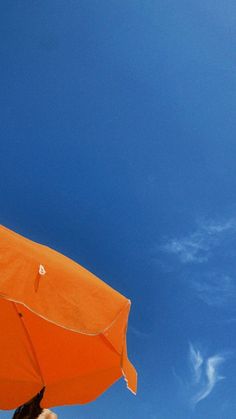 an orange umbrella is in the air with a blue sky behind it and white clouds