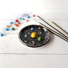 two chopsticks sitting on top of a black plate with planets and stars in it